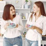 Two women enjoying tea beside a decorative cake stand in a stylish kitchen setting