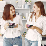 Two women enjoying tea with floral cups next to a stylish cake stand in a chic boutique kitchen