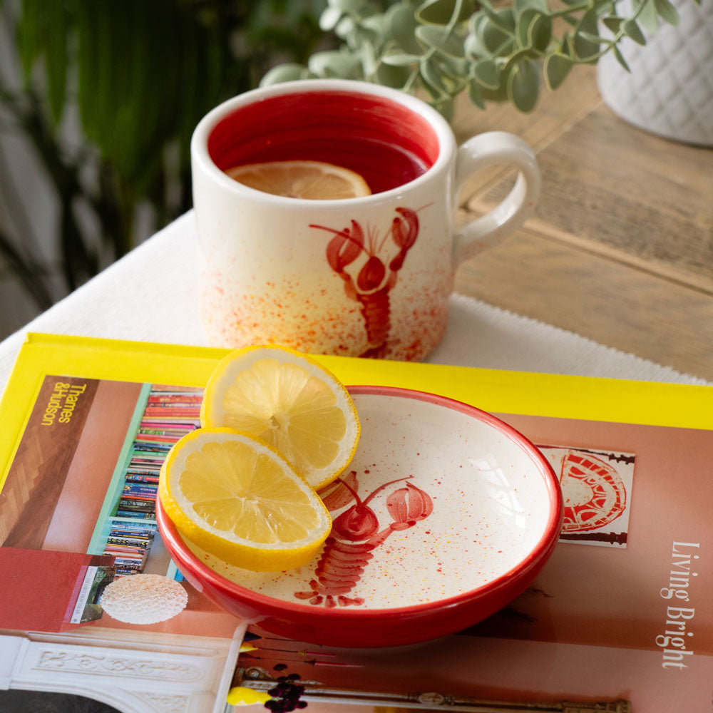 Selbrae House Ceramic Mug with Lobster Design and Butter Dish with Lemon Slices on a Magazine