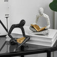 Two artistic ornaments reading books, one black and one white, on a stylish tabletop