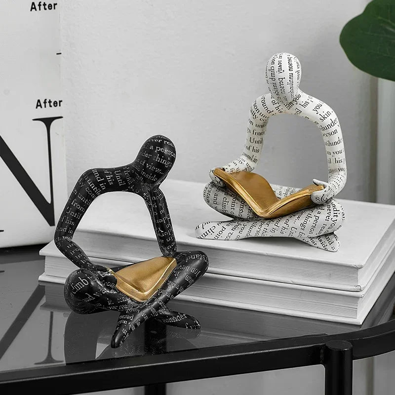 Two artistic ornaments reading books, one black and one white, on a stylish tabletop