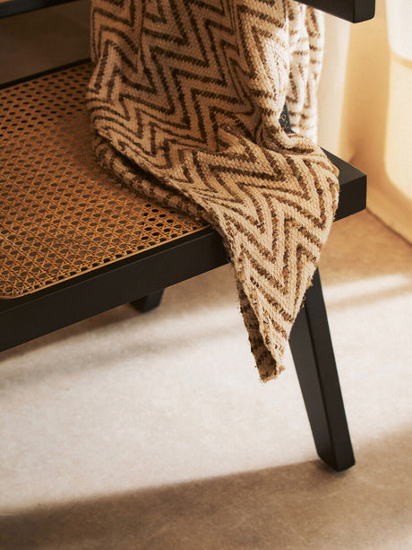 Orsina Dining Chair with a woven cane seat and a stylish patterned throw draped over it