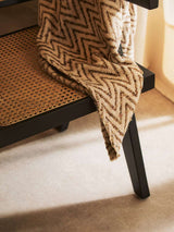 Orsina Dining Chair with a woven cane seat and a stylish patterned throw draped over it