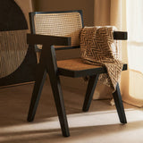 Orsina Dining Chair with a modern black frame and natural woven seat, styled with a cosy blanket