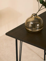 Stylish Orsina Dining Table with a sleek black surface and elegant legs, featuring a decorative glass vase