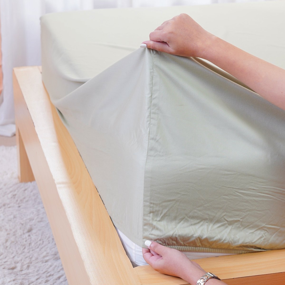 Light green fitted sheet from SHEET STORY being placed on a wooden bed frame