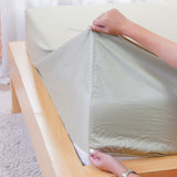 Light green fitted sheet from SHEET STORY being placed on a wooden bed frame