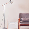 Modern Orsina Floor Lamp featuring a sleek design with a metallic shade and wooden accent next to a stylish armchair