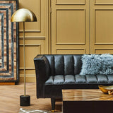 Orsina Floor Lamp with a sleek gold shade and stylish base beside a modern black sofa