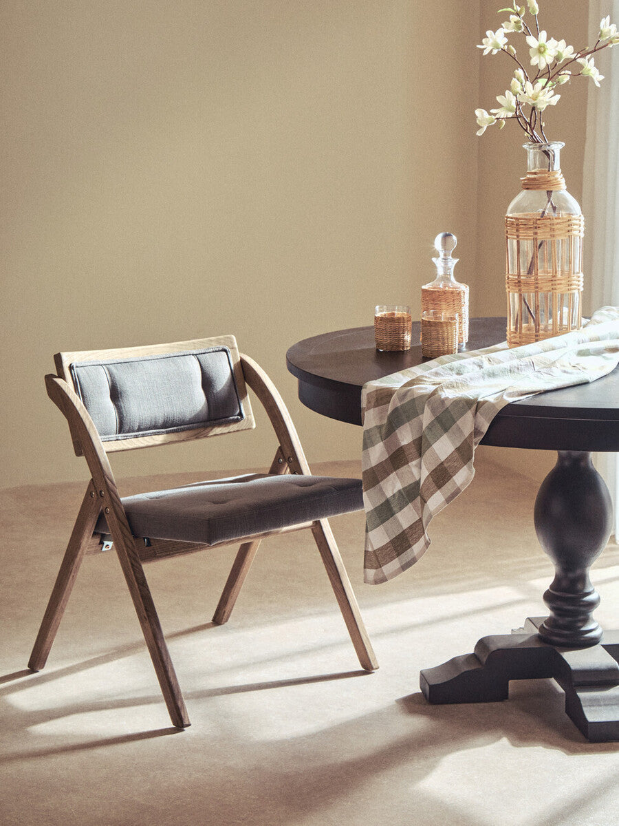 Orsina Folding Chair with a wood frame and cushioned seat, placed beside a stylish dining table
