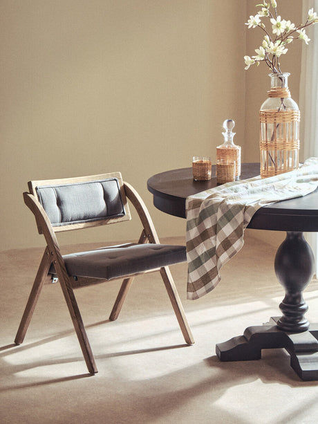 Orsina Folding Chair with a wood frame and cushioned seat, placed beside a stylish dining table