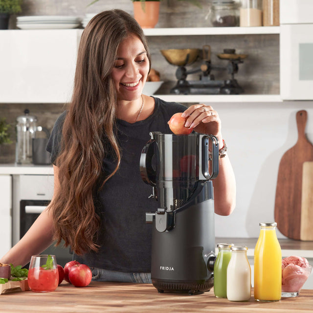 Fridja Fruit Juicer being used by a woman with fresh apples and juice bottles on the kitchen counter