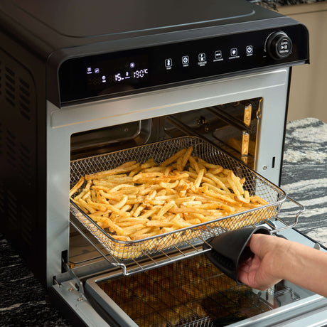 Fridja Digital Air Fryer with crispy golden fries in the oven and user holding an oven mitt