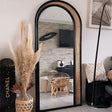 Elegant arched Nisu Home mirror with a black frame and natural rattan accents in a stylish interior