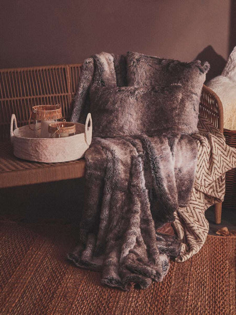 Orsina Fur Cushion placed on a rattan sofa with a cozy throw blanket and decorative accessories