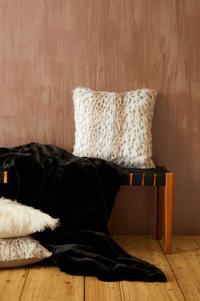 Orsina Fur Throw in black draped on a wooden bench with stylish faux fur cushions