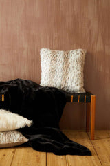 Orsina Fur Throw in black draped on a wooden bench with stylish faux fur cushions
