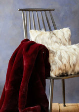 Luxurious burgundy Fur Throw draped over a modern chair, paired with fluffy cushions