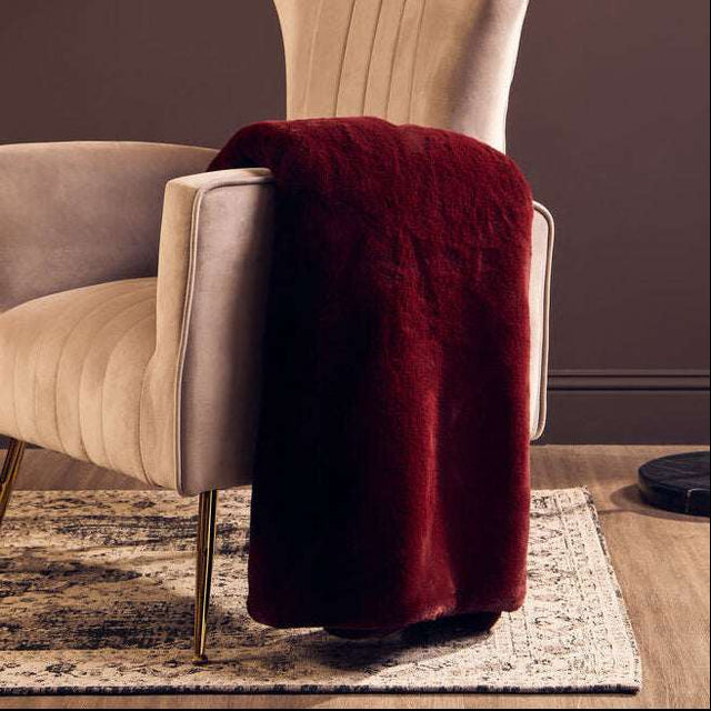Orsina Fur Throw in rich burgundy draped over a stylish armchair for a cosy home decor touch