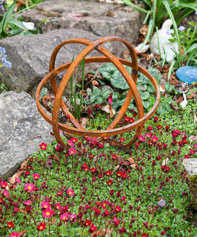 Rustic metal Garden Sphere Ornaments enhancing a garden with vibrant flowers and rocks