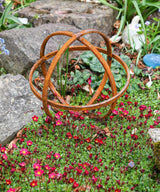 Rustic metal Garden Sphere Ornaments enhancing a garden with vibrant flowers and rocks