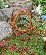 Rustic metal Garden Sphere Ornaments enhancing a garden with vibrant flowers and rocks