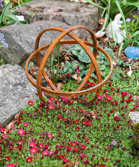 Rustic metal Garden Sphere Ornaments enhancing a garden with vibrant flowers and rocks