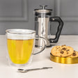 Bialetti double-walled glass mug with herbal tea, beside a French press and cookies, perfect for enjoying glass mugs