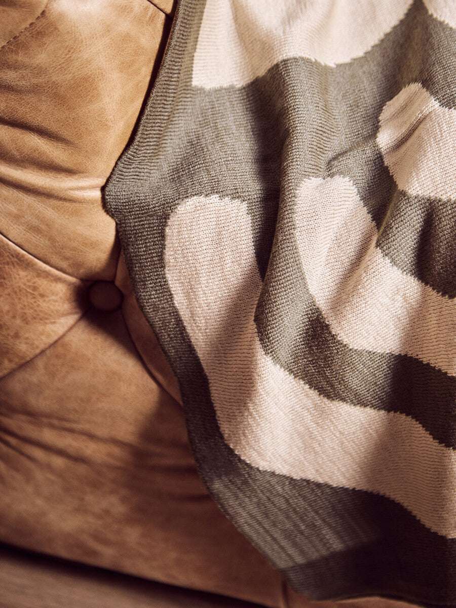 Orsina Green Throw with a modern pattern draped over a stylish beige sofa