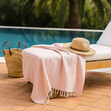 Orsina Hammam Towel in soft pink, draped over a sunbed with a straw hat and woven basket nearby