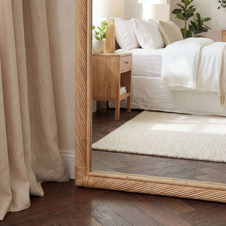 Large wooden frame mirror reflecting a bright bedroom with natural light and greenery