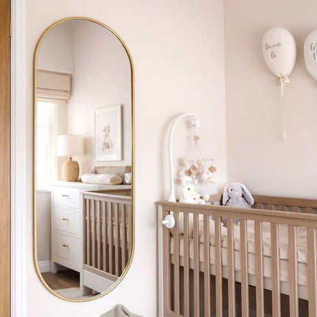 Elegant Jobu Home Oval Mirror in gold frame, reflecting a stylish nursery with a cot