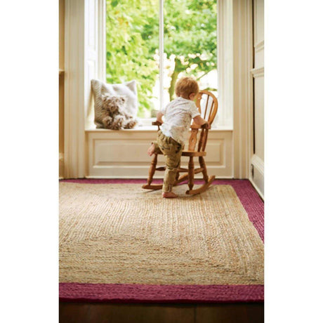 Child playing on a Jute Rug with a pink border in a sunlit room by the window