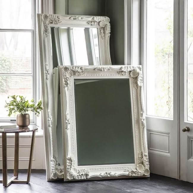 Elegant white Leaner Mirror with ornate frame stacked against a wall in a bright room