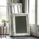 Elegant white Leaner Mirror with ornate frame stacked against a wall in a bright room