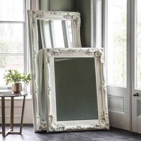 Elegant white Leaner Mirror with ornate frame stacked against a wall in a bright room