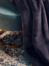 Orsina Fur Throw in dark colour draped over a plush stool on a patterned rug
