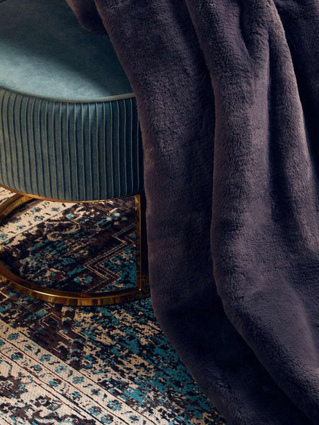 Orsina Fur Throw in dark colour draped over a plush stool on a patterned rug
