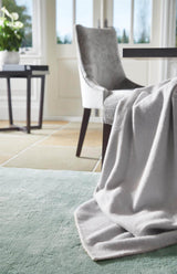 Luxurious grey Luxury Rug placed under a dining chair in a bright interior setting