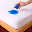 SHEET STORY Mattress Protector showcasing water resistance with blue liquid spilled on a soft surface
