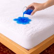 SHEET STORY Mattress Protector showcasing water resistance with blue liquid spilled on a soft surface