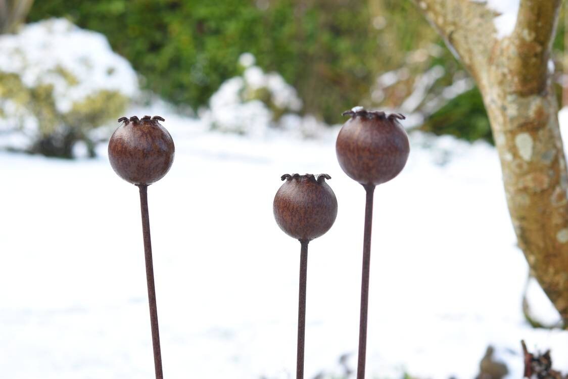 Three decorative Metal Poppy Seedhead garden stakes with detailed textures against a snowy backdrop