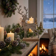Stylish metal reindeer decoration on a festive mantel adorned with candles and pinecones