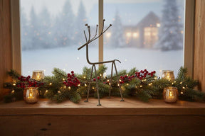 Decorative Metal Reindeer on a window sill surrounded by holiday foliage and lanterns