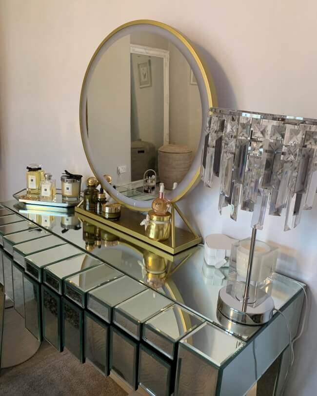 Elegant Hollywood mirror with a round design and gold frame, displayed on a stylish mirrored dressing table