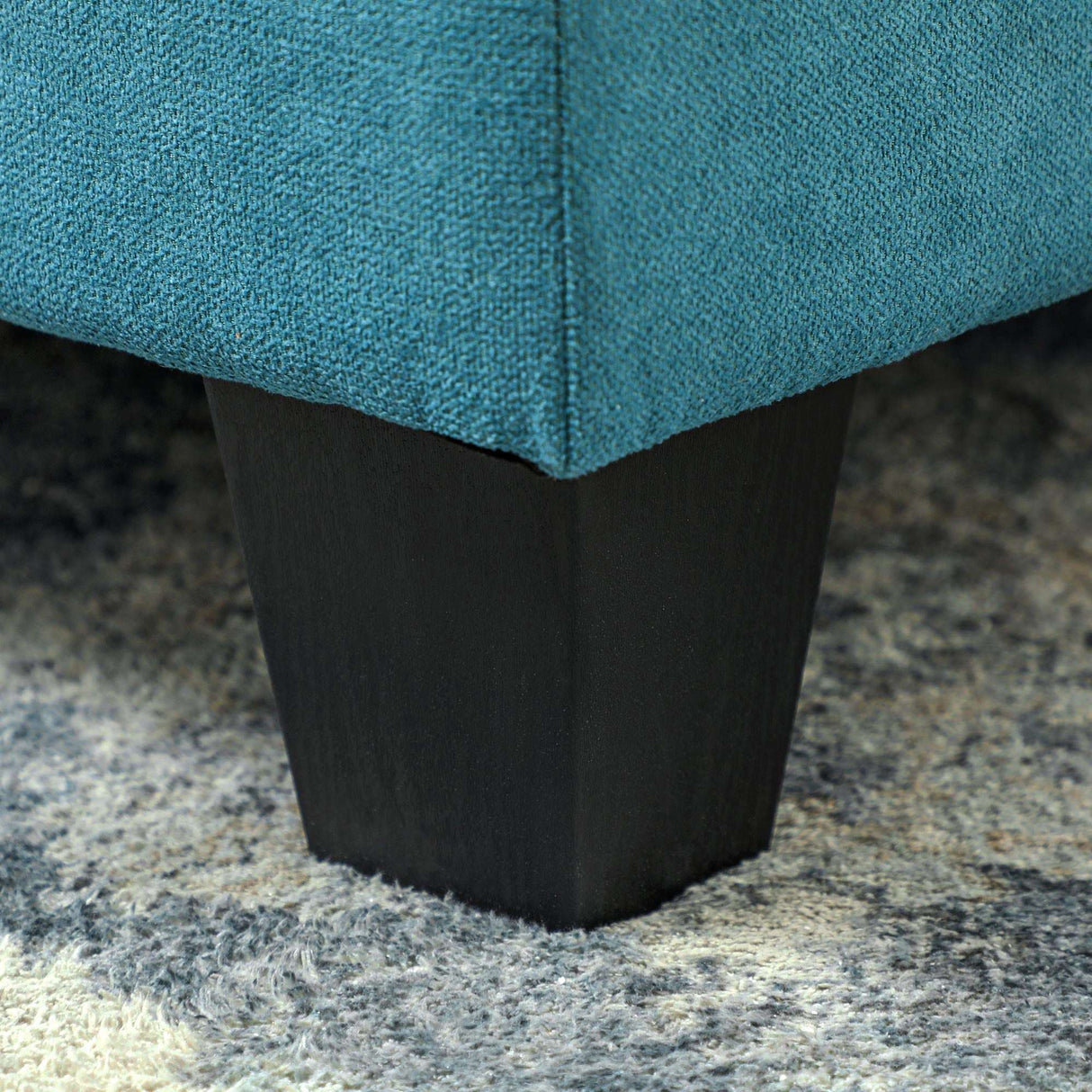 Close-up of a Modula Sofa leg with a dark wood finish against a soft rug