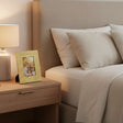 Orsina gold photo frame on bedside table next to lamp, displaying a family picture in a cozy bedroom