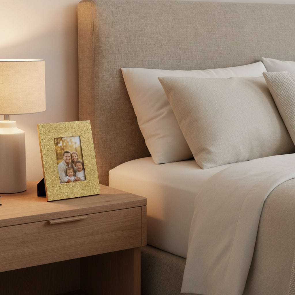Orsina gold photo frame on bedside table next to lamp, displaying a family picture in a cozy bedroom