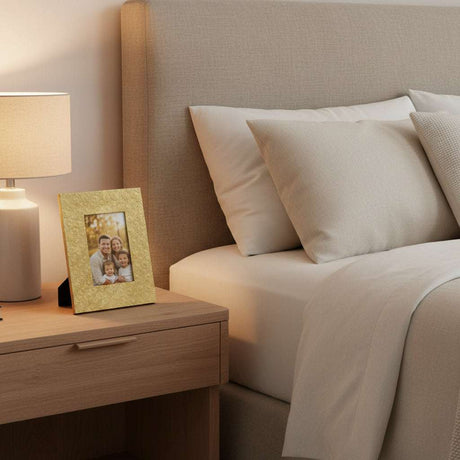 Orsina gold photo frame on bedside table next to lamp, displaying a family picture in a cozy bedroom