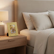 Orsina gold photo frame on bedside table next to lamp, displaying a family picture in a cozy bedroom